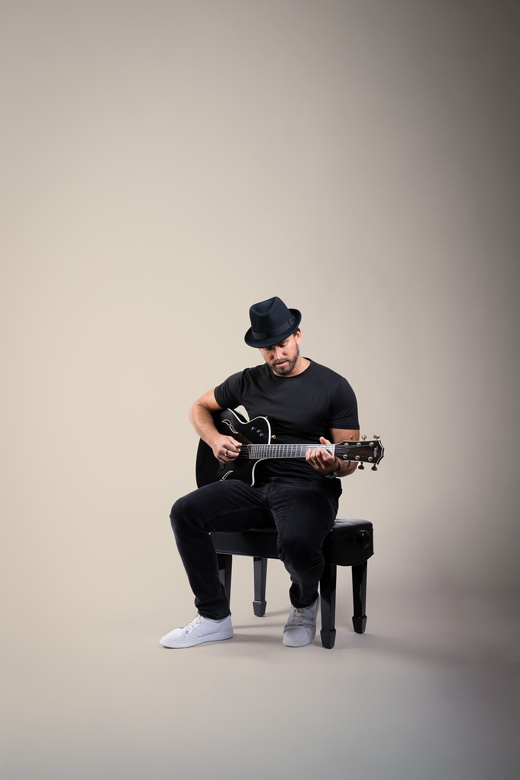 Ryan Hiller seated with a black guitar against a beige background
