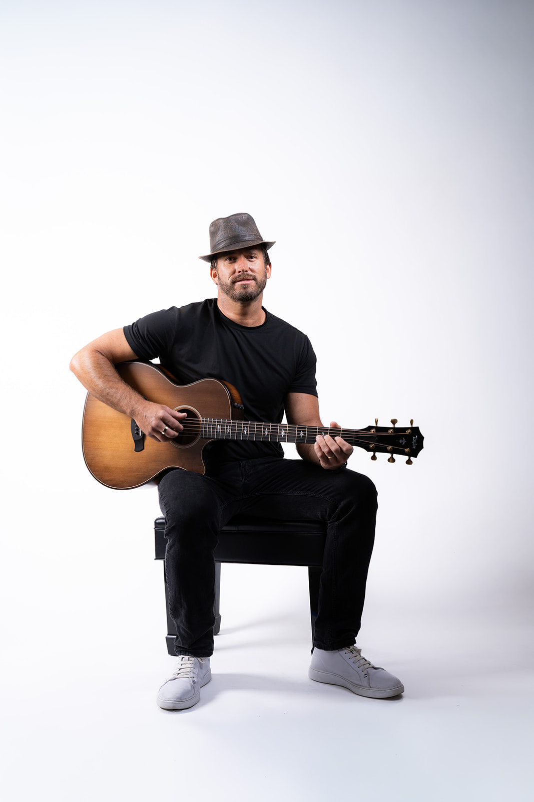 Ryan Hiller seated with an acoustic guitar on a light background